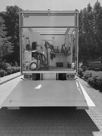 Mobiele werktruck met open laadklep waarin gespecialiseerde rioolrenovatie‑ en inspectieapparatuur staat opgesteld, inclusief slangen, bedieningsunits en technische opstelling voor reliningswerken.