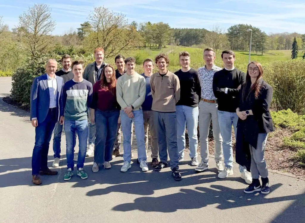 Groepsfoto van de Renotec Junior Board 2025, genomen buiten op een zonnige dag. De groep staat samen op een asfaltpad met groen, bomen en een open landschap op de achtergrond